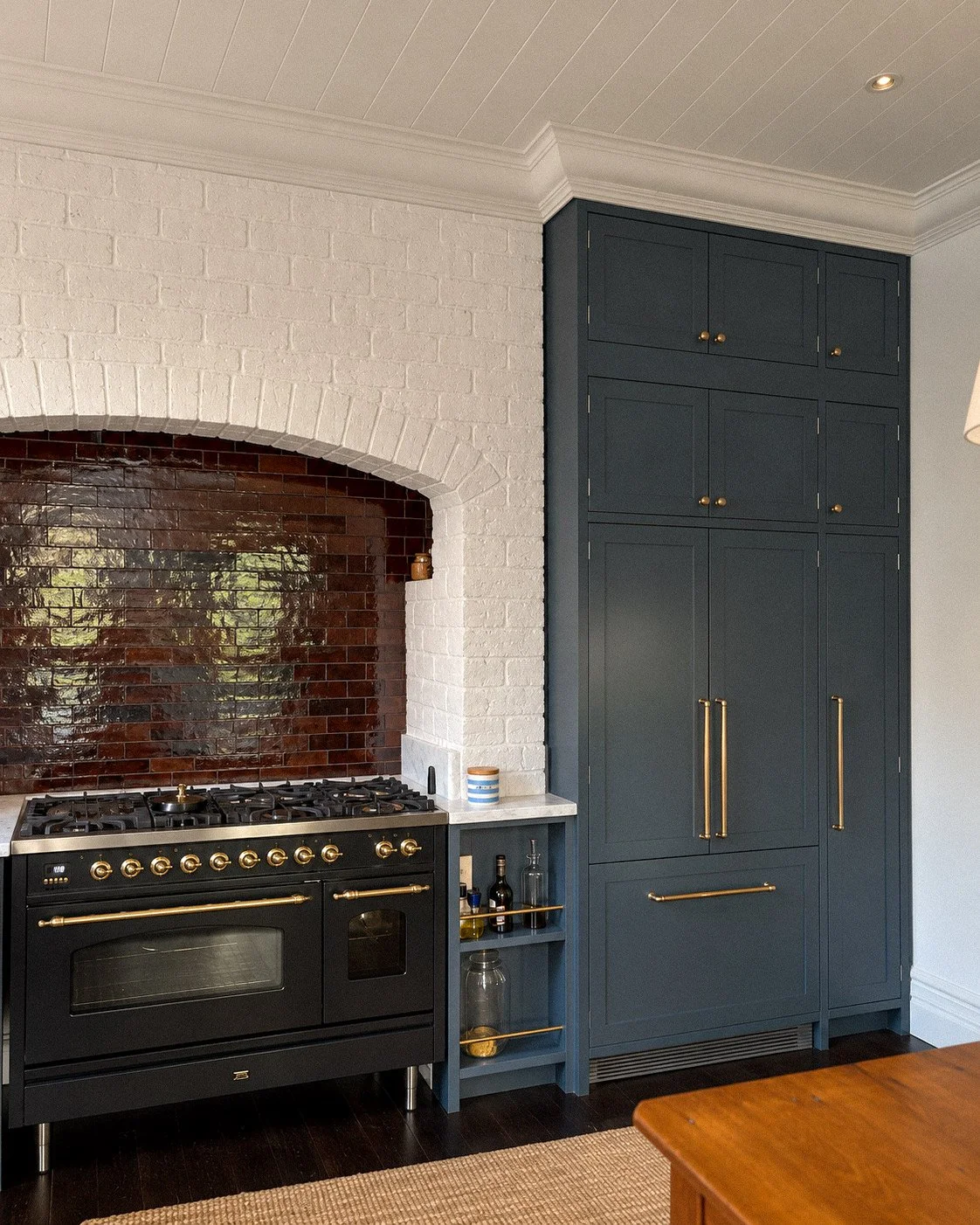 Kitchen with a black oven and dark blue cabinetry, white brick arch, and a backsplash of reflective brown tiles.