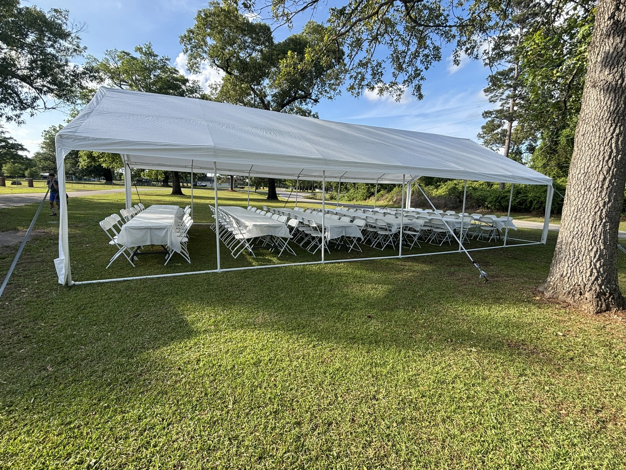 White event tent with tables and chairs set up on a grassy area near trees, under a blue sky with scattered clouds.