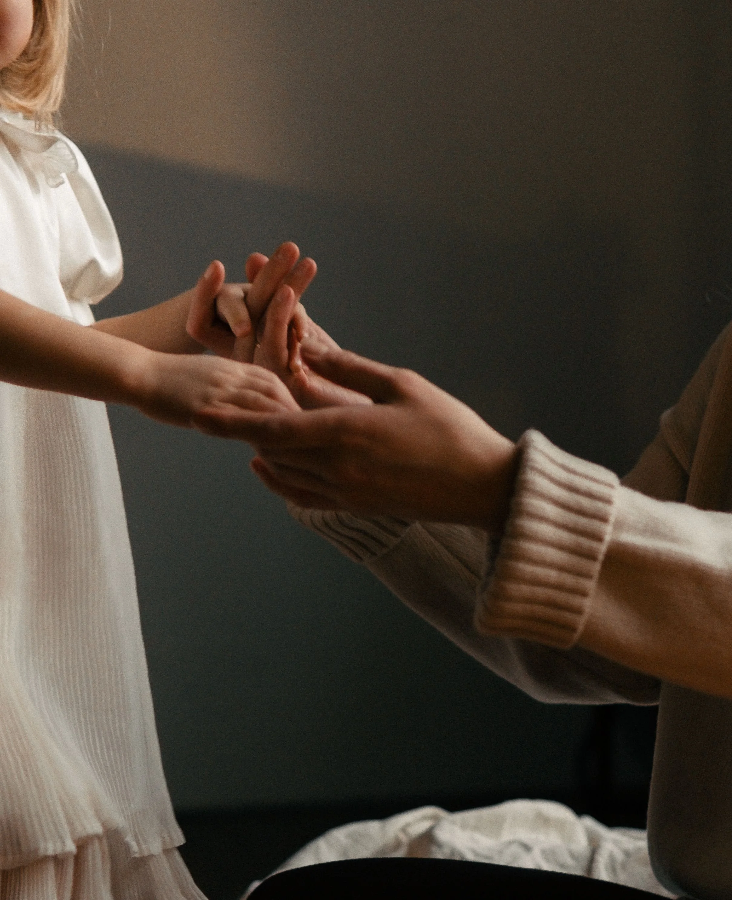 Close-up of two people holding hands, one wearing a white long-sleeve sweater and the other in a light-colored blouse with pleats.