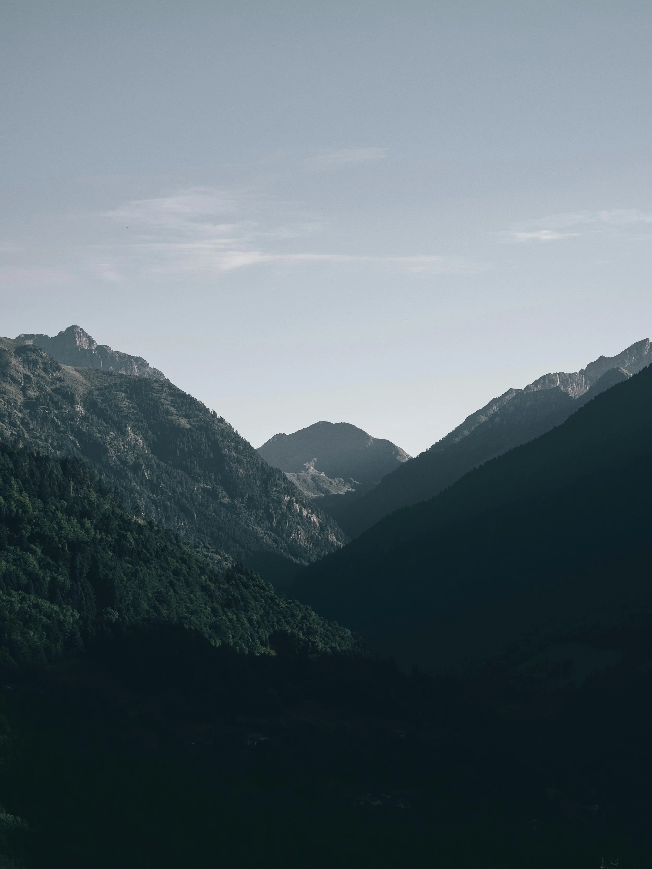 View of green forested mountain range with rugged peaks under a partly cloudy sky.