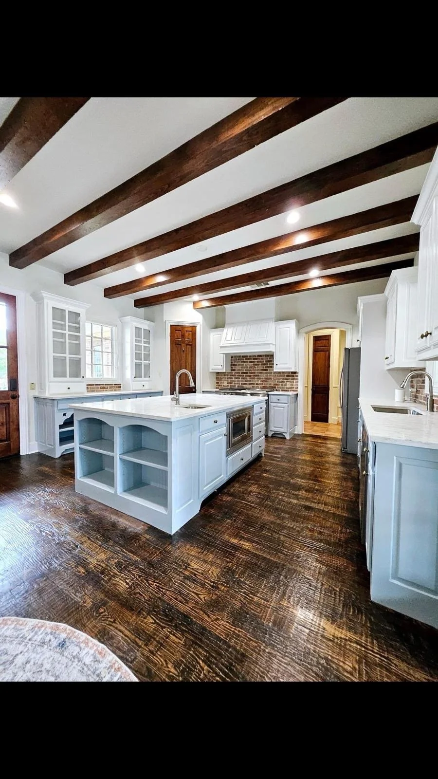 Modern farmhouse kitchen with white cabinets, dark wood flooring, and exposed ceiling beams.