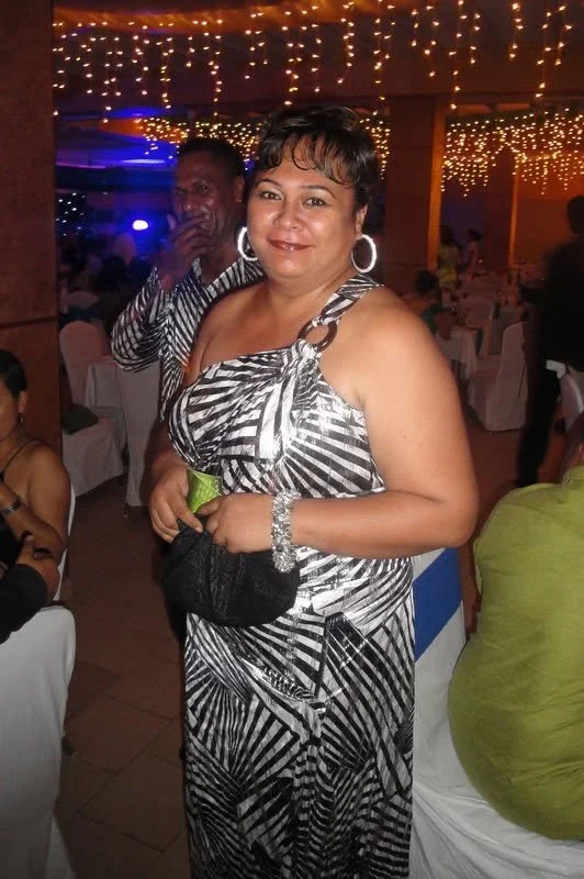 A woman in a black and white patterned dress at a party or celebration, holding a small purse and a lime, with festive string lights overhead.