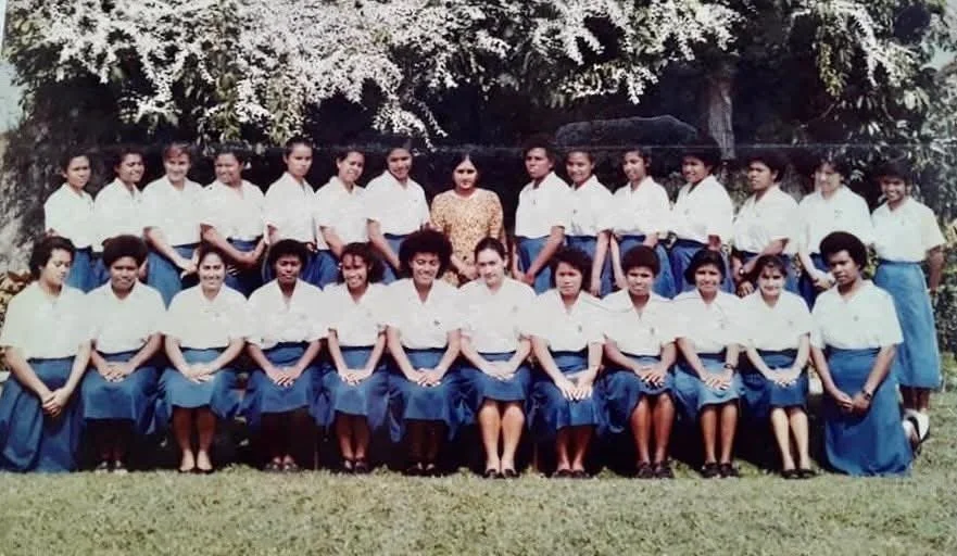A group of young women in school uniforms posing outdoors with trees in the background.