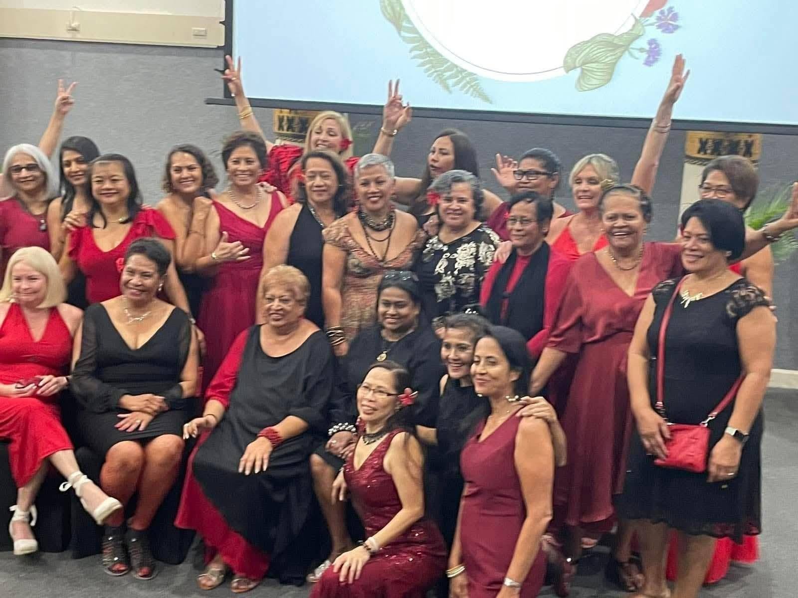 Group of women dressed in red and black, posing together at a celebration or event.