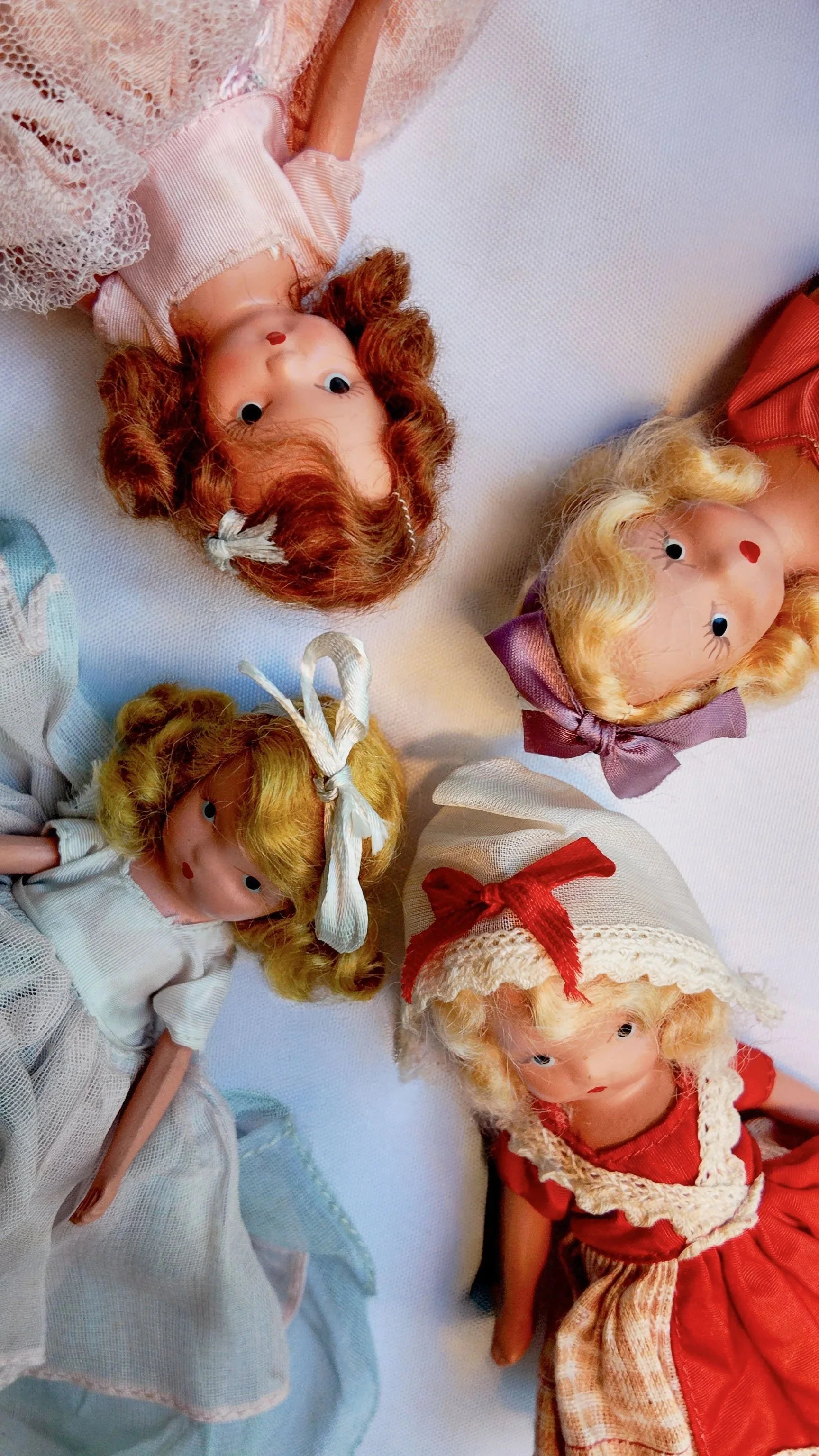 Four vintage Barbie dolls with curly hair, dressed in old-fashioned clothing, lying on a white surface.