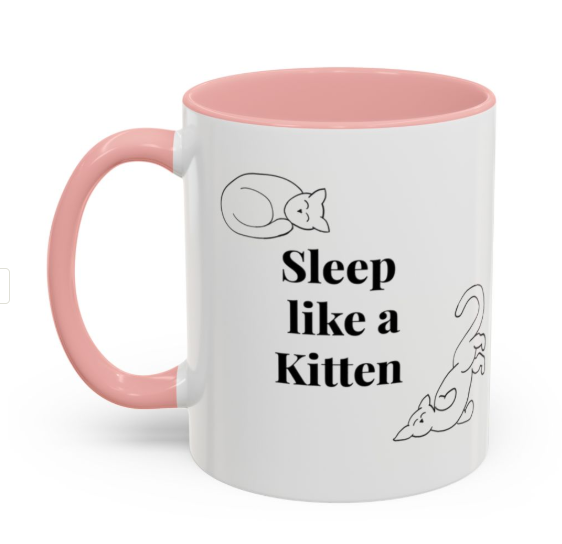 White ceramic mug with pink interior and handle, featuring black text that reads 'Sleep like a Kitten' and illustrations of a curled-up kitten and a playful kitten.