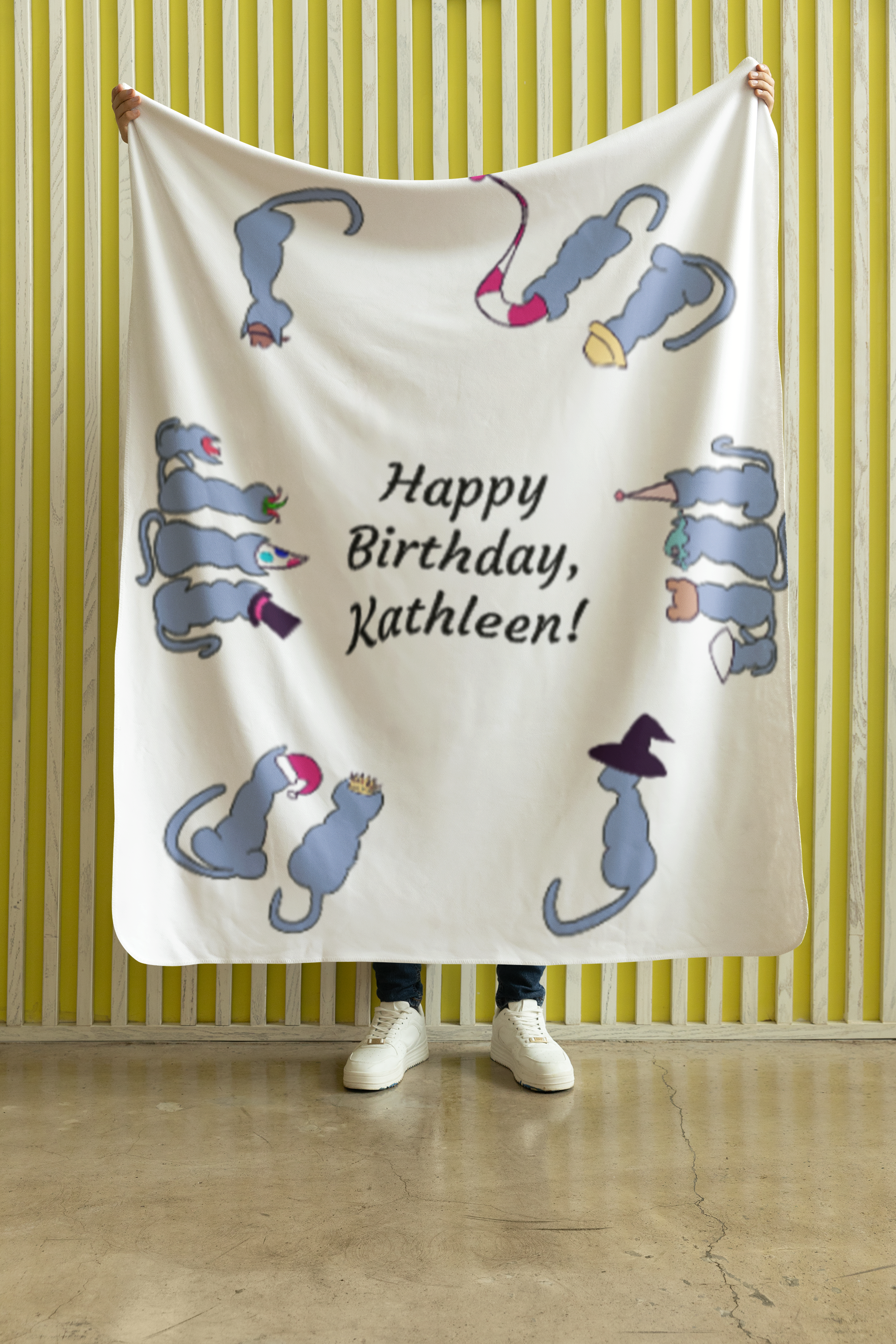 Person holding a birthday banner with cartoon mice and the message 'Happy Birthday, Kathleen!' in front of a yellow striped wall.