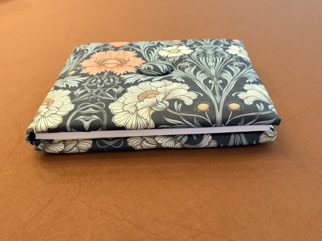A closed floral patterned laptop sleeve or case resting on a brown surface.