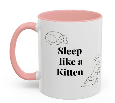 White mug with pink interior and handle, featuring a sleeping cat illustration, a playful kitten drawing, and the text "Sleep like a Kitten" in bold black letters.