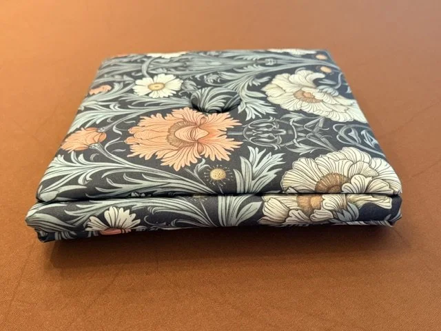 Folded fabric with a floral pattern featuring large flowers in white, cream, and pink on a dark background, placed on a wooden surface.