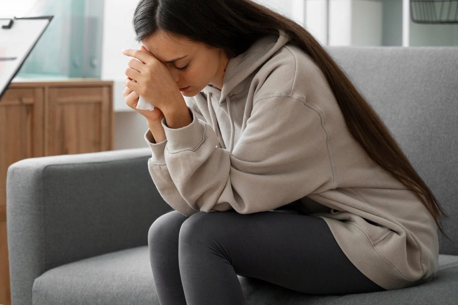A woman sitting on a couch with her head in her hands, appearing distressed or upset.