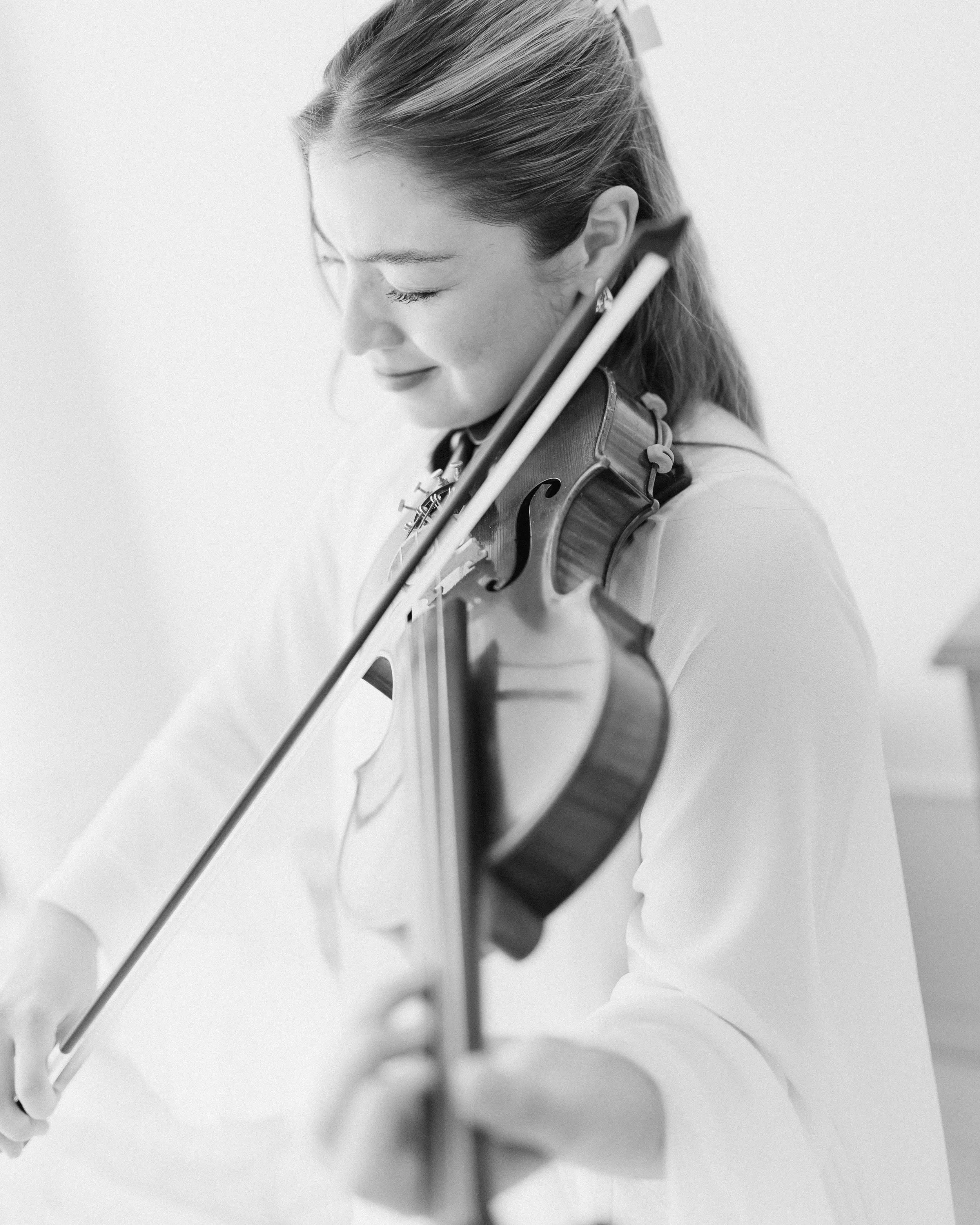 Black and white photo of a woman with closed eyes playing a violin with focus on her face and the instrument.