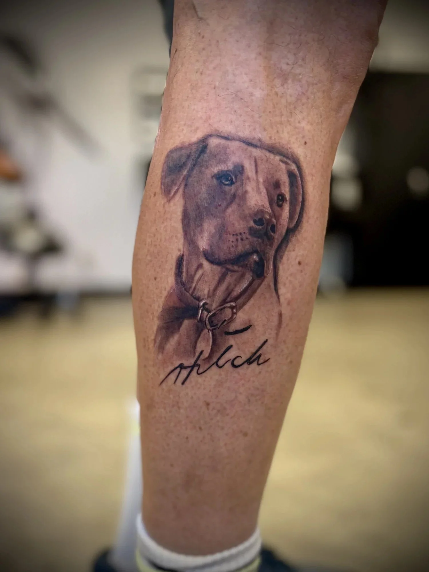 Black and grey memorial dog portrait tattoo with name script on calf, by Esteban Tattoos in San Diego
