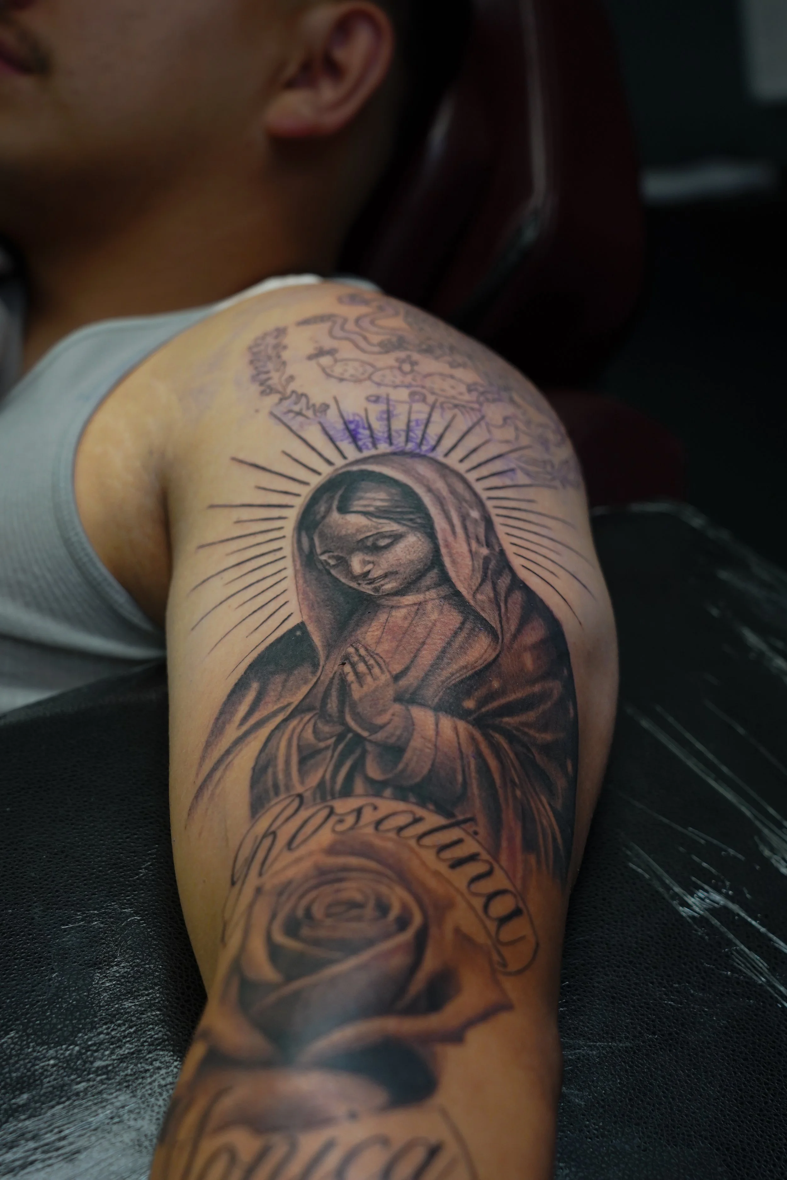 Tattoo of the Virgin Mary with hands in prayer on a person's upper arm.