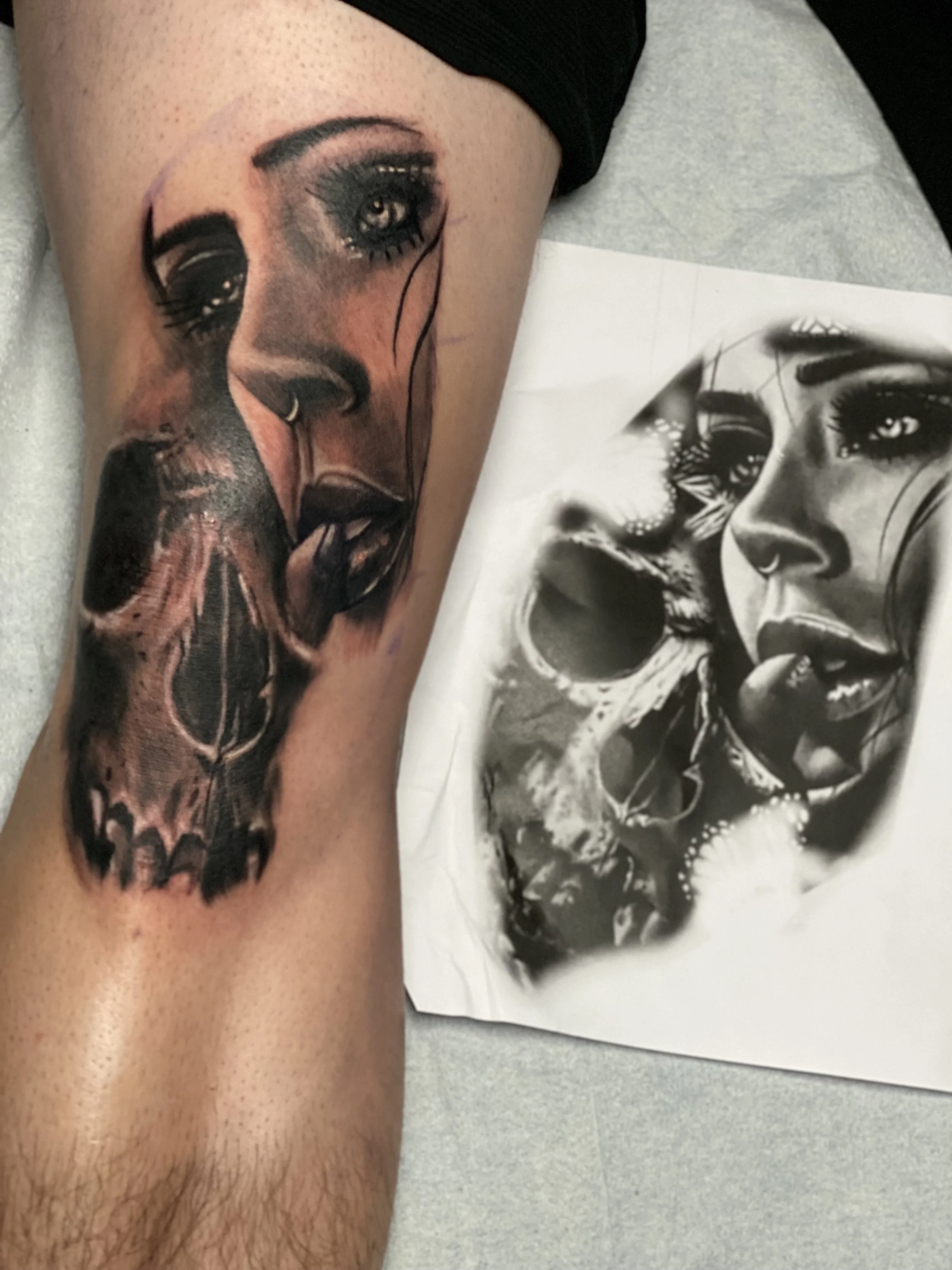 Realistic black and gray portrait tattoo of a woman's face on a person's thigh, with a printed reference image of the same face beside it.