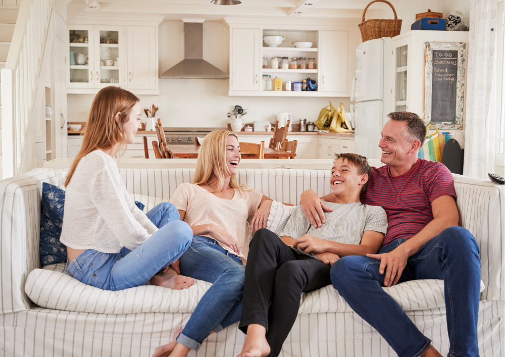 A family of four, including two kids, sitting on a striped sofa in a cozy kitchen, laughing and enjoying their time together.