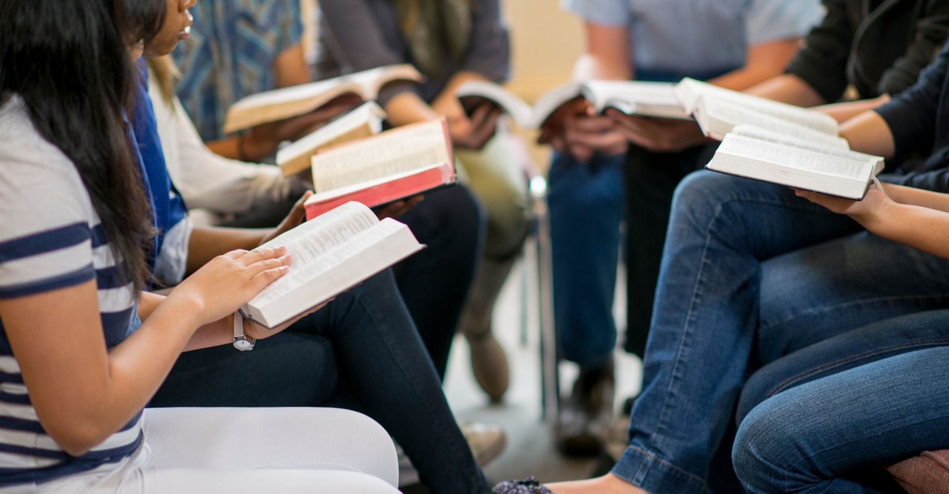 A group of people sitting in a circle, holding and reading open books, likely participating in a group study or discussion.