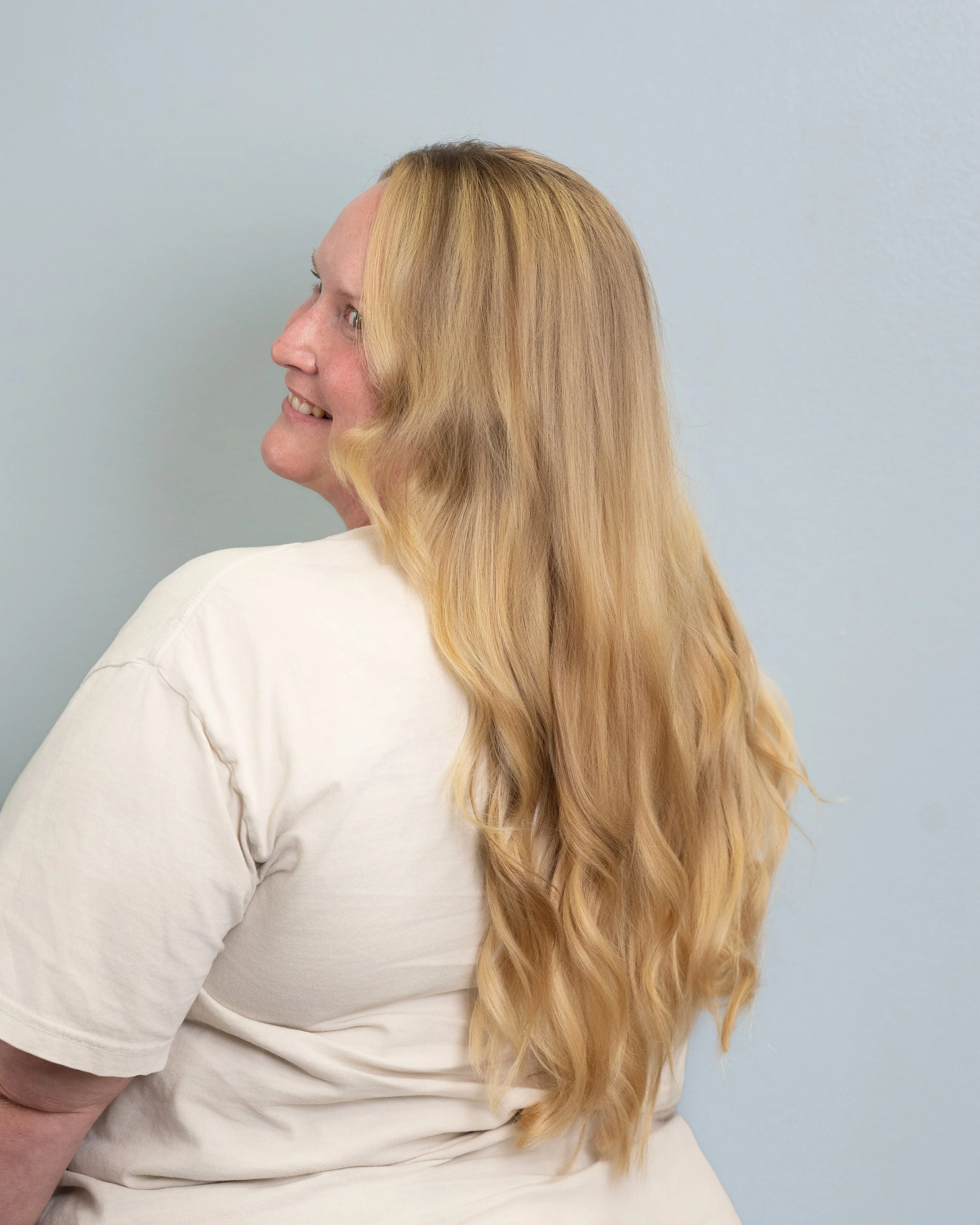 Side view of a woman with long blonde hair wearing a white shirt against a light blue wall.