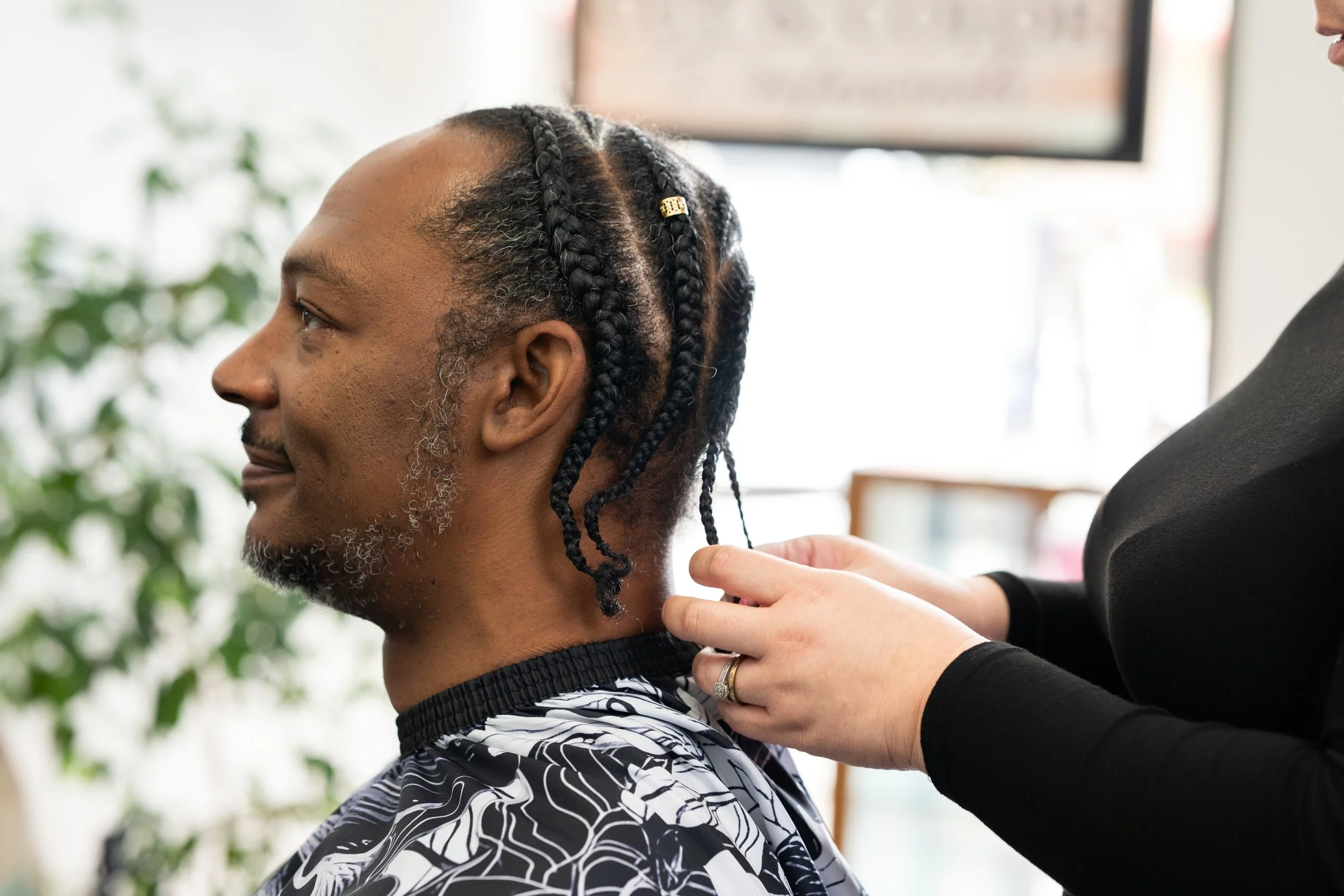 A man receiving a haircut in a salon, with a barber or hairstylist adjusting his hair.