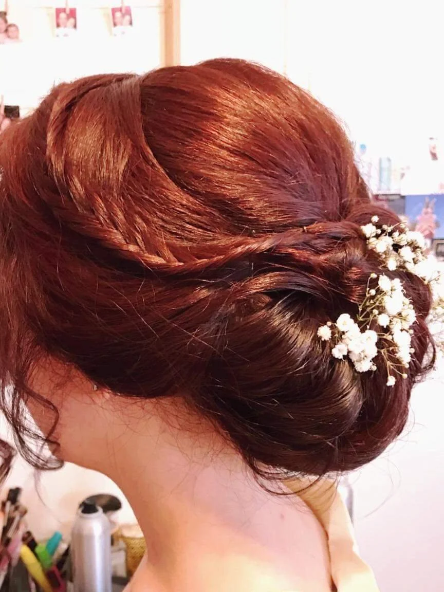 A woman's updo hairstyle decorated with white baby's breath flowers.