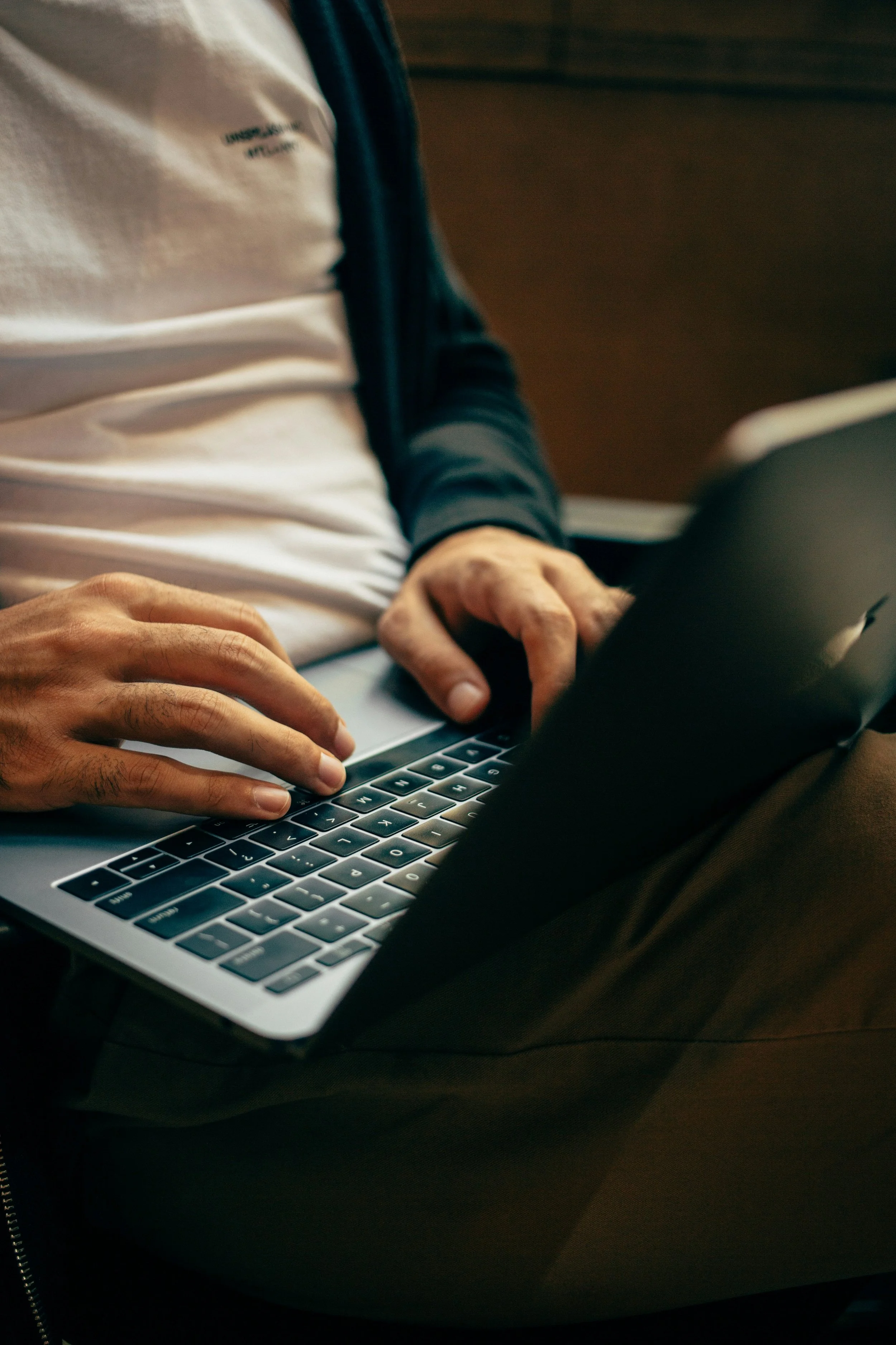 Person working on a laptop, wearing a white shirt with blue sleeves and sitting at a desk.