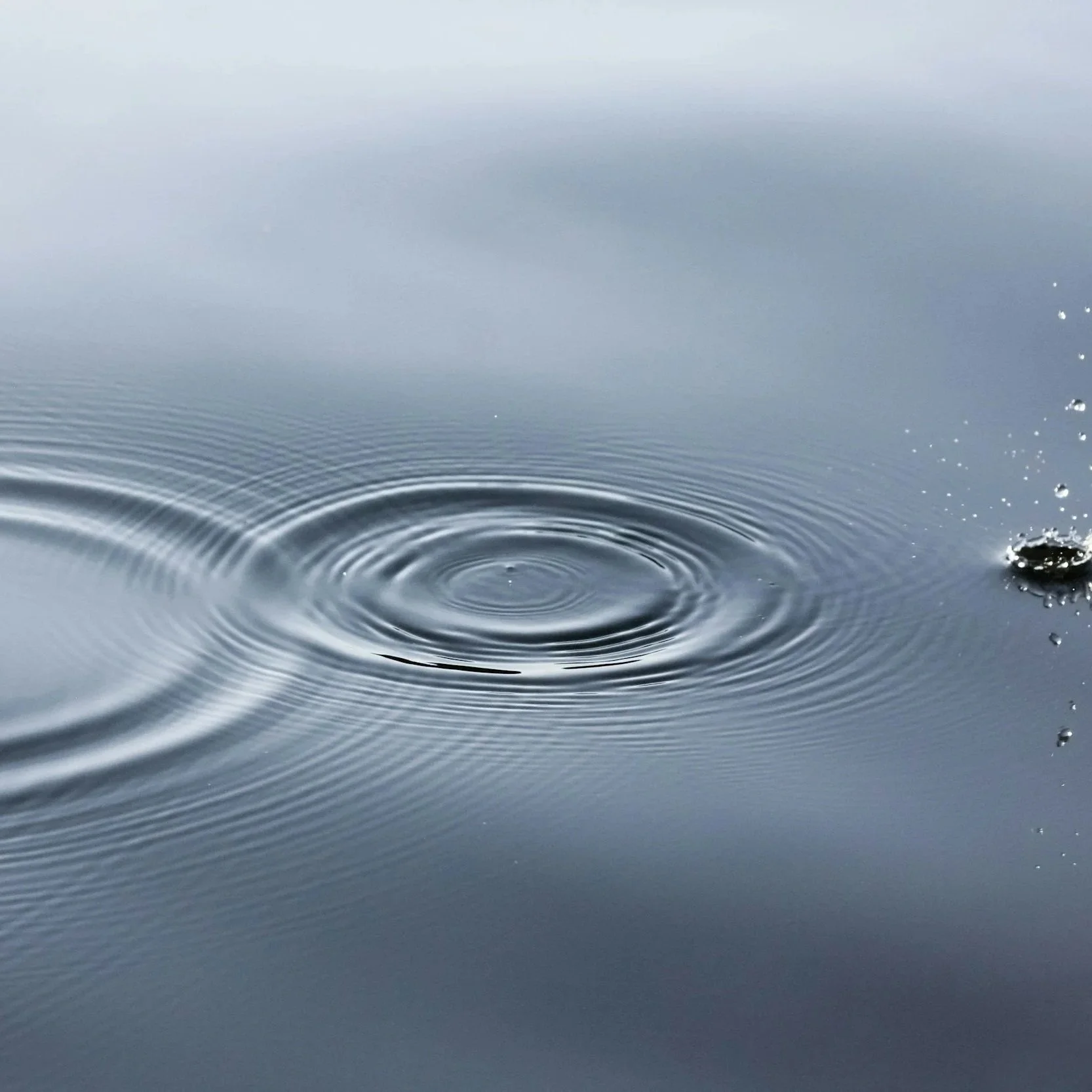 Close-up of a water droplet hitting a calm water surface, creating ripples.