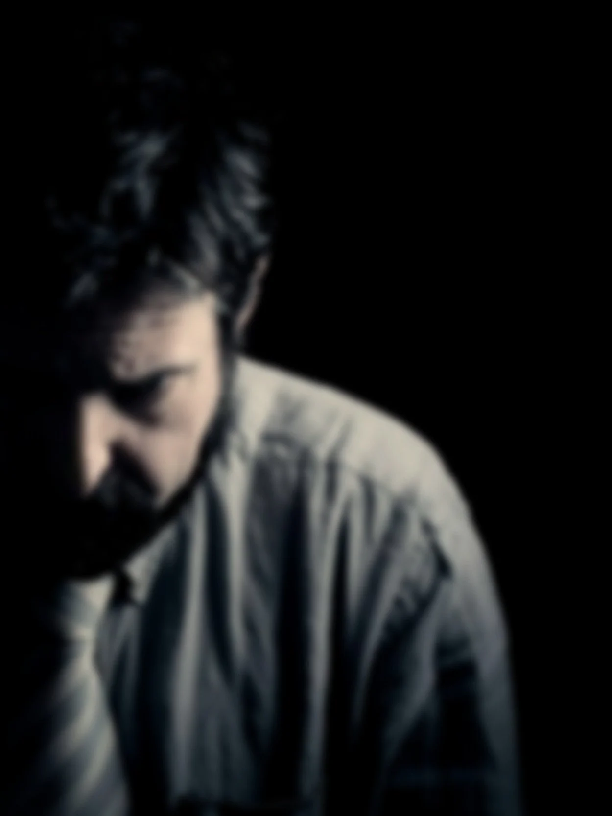 A person with dark hair looking downward, feeling shame potentially, sad, wearing a light-colored striped shirt against a dark background.