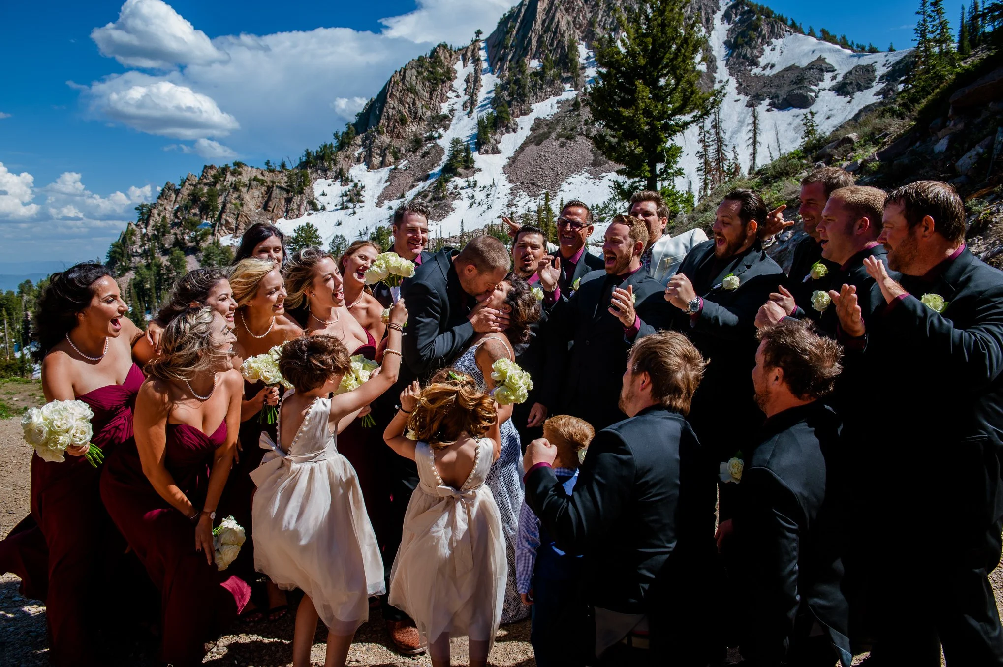 Large wedding party celebrates together with snow-capped mountains rising behind them at Snowbasin.