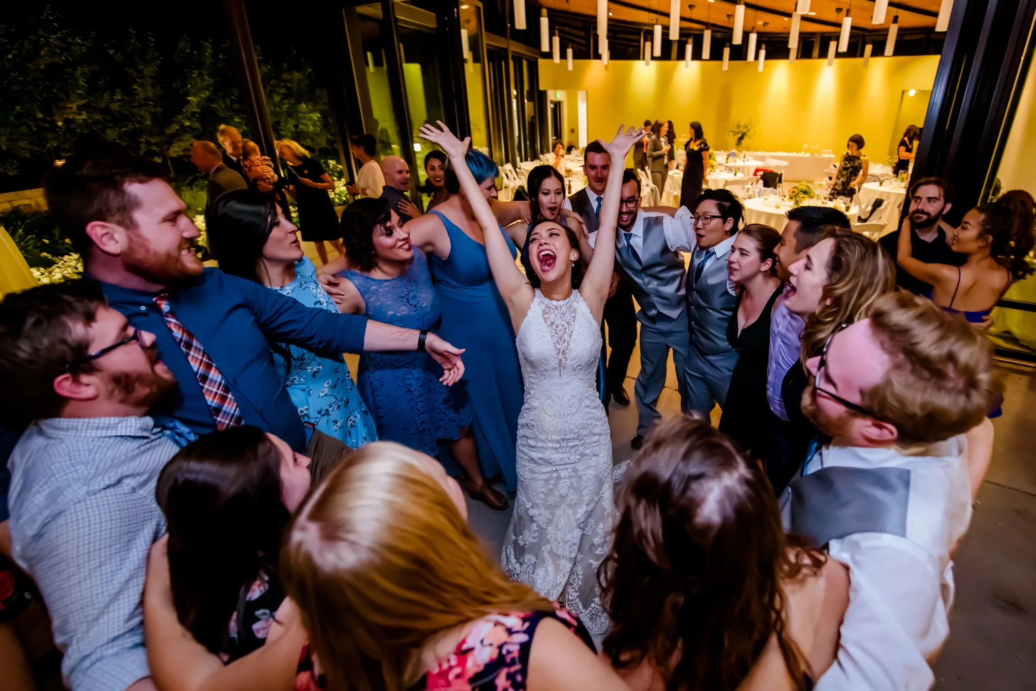 Bride throws her arms up laughing while surrounded by bridesmaids and groomsmen on the dance floor.