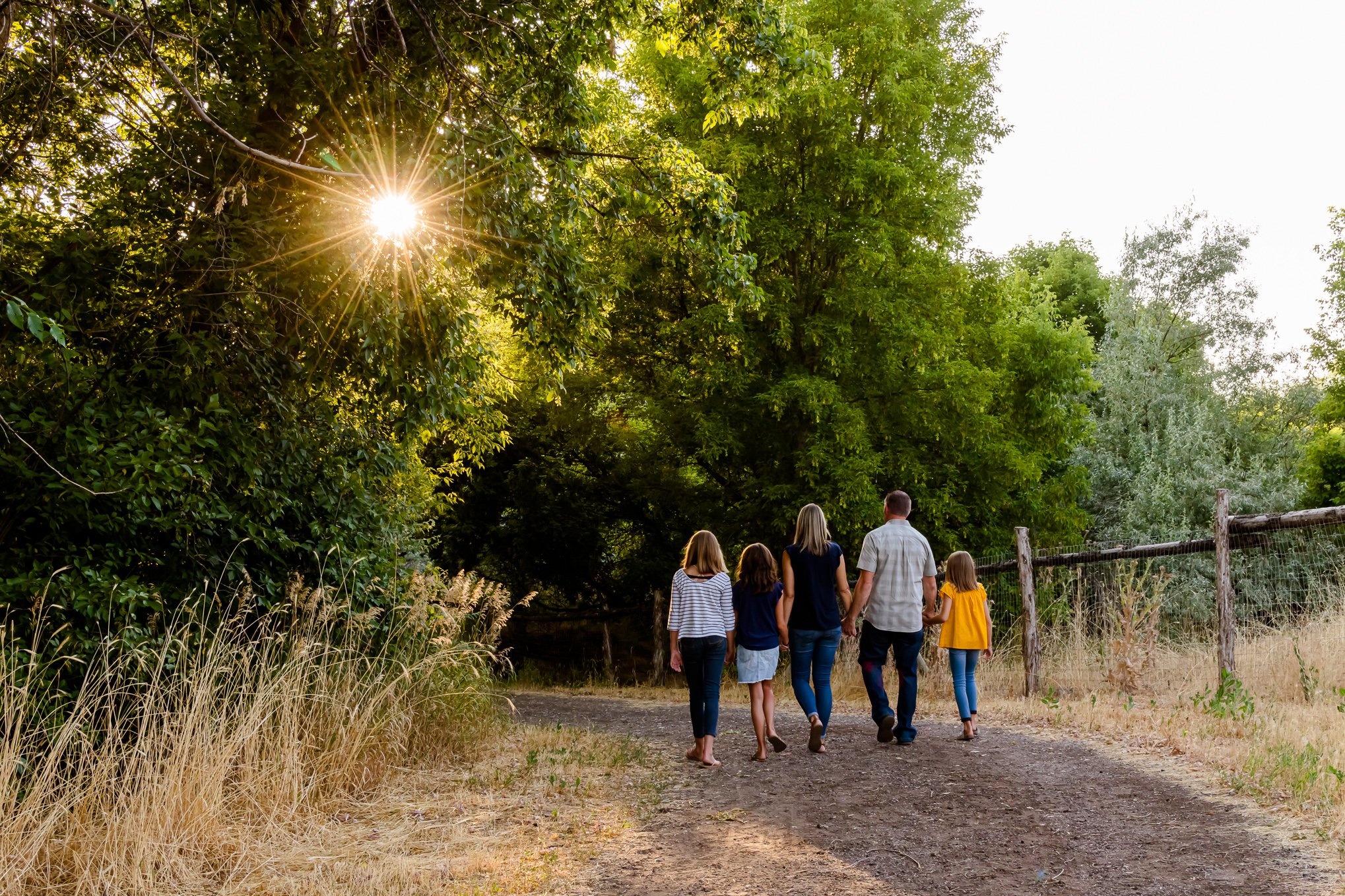 A family walks on a dirt path toward the sunset