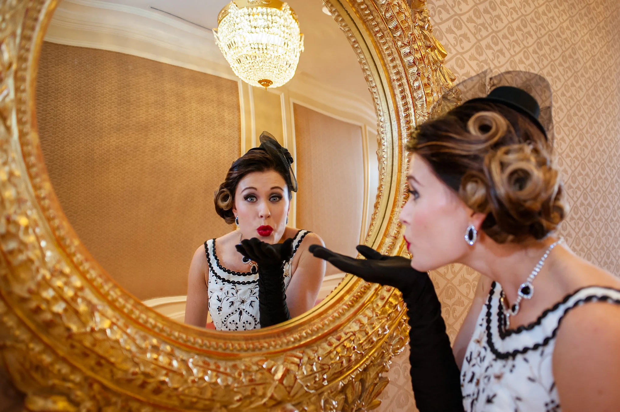 Bride at Grand America blows a kiss into the gold mirror with chandelier in the background.