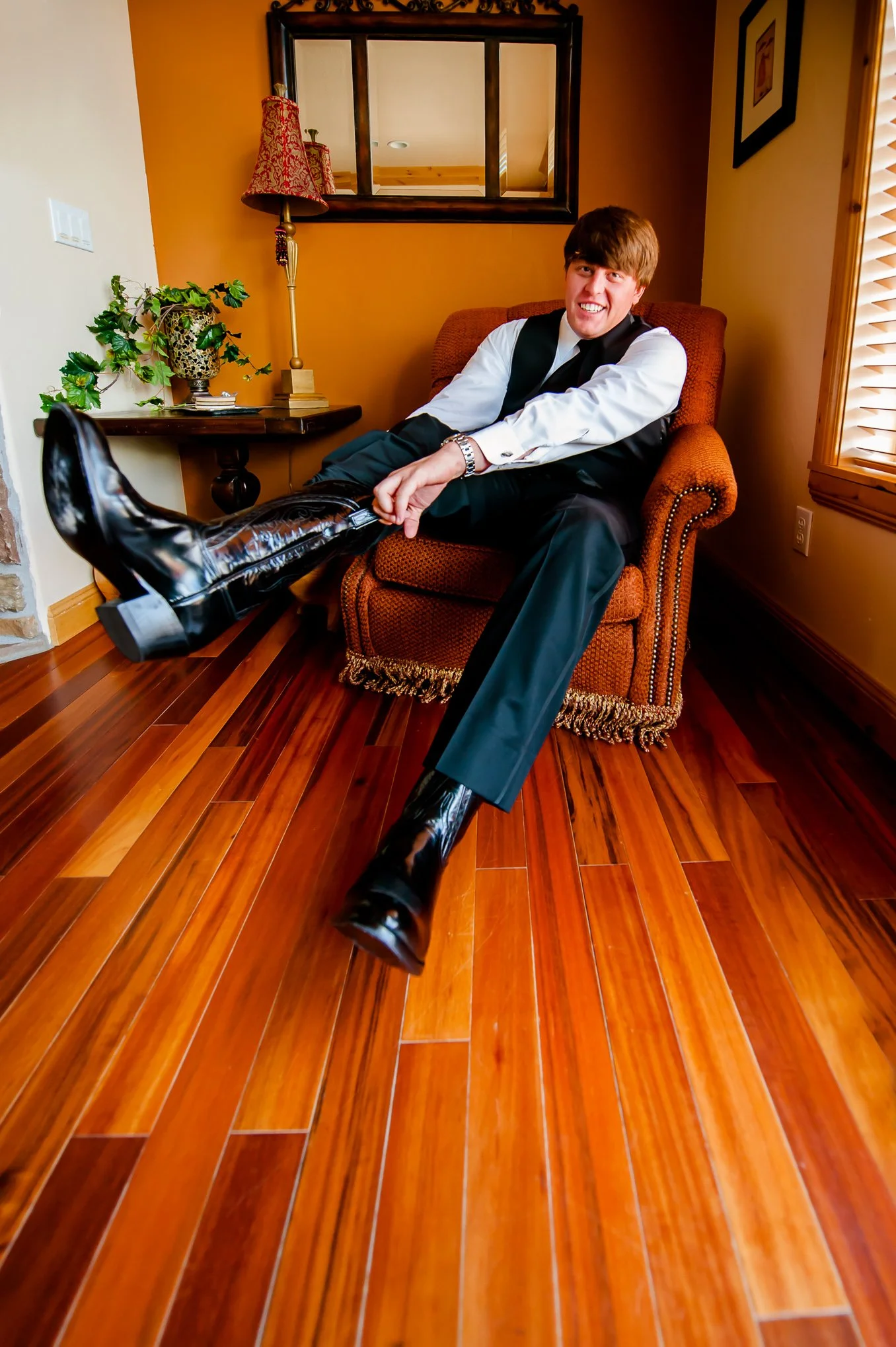 Groom relaxes in an armchair showing off his black cowboy boots while getting ready for his wedding.