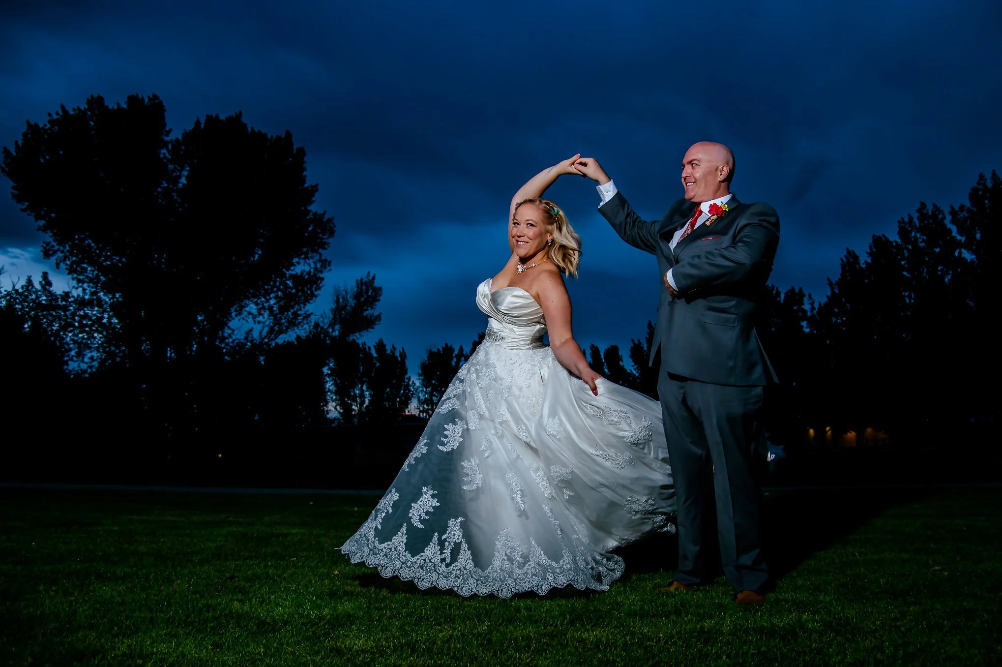 Bride and groom share a twirl at dusk with dramatic storm clouds behind them.