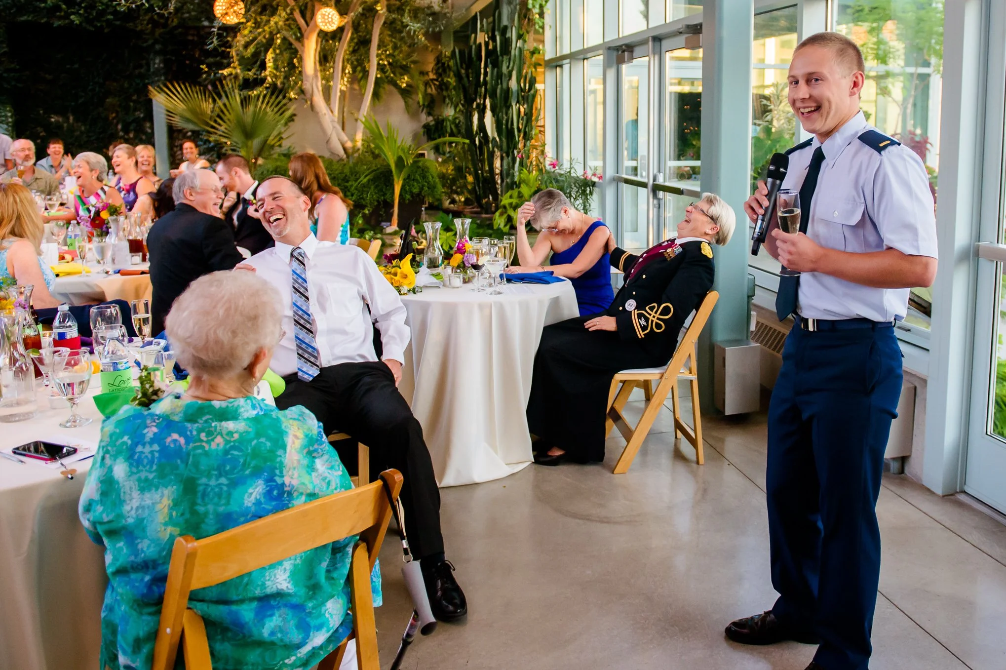 A groomsman gives a toast while guests burst into laughter at a Salt Lake Valley wedding reception.