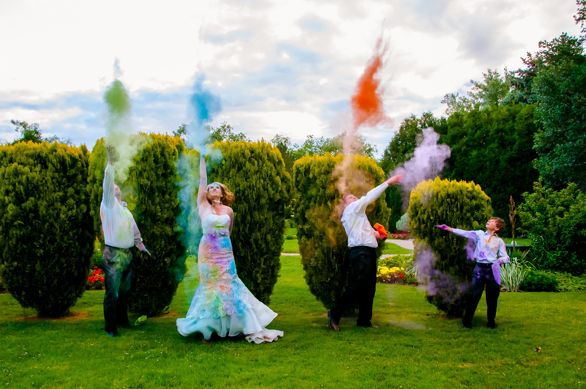 Bride, groom and their two boys throw colored chalk in the air making themselves colorful