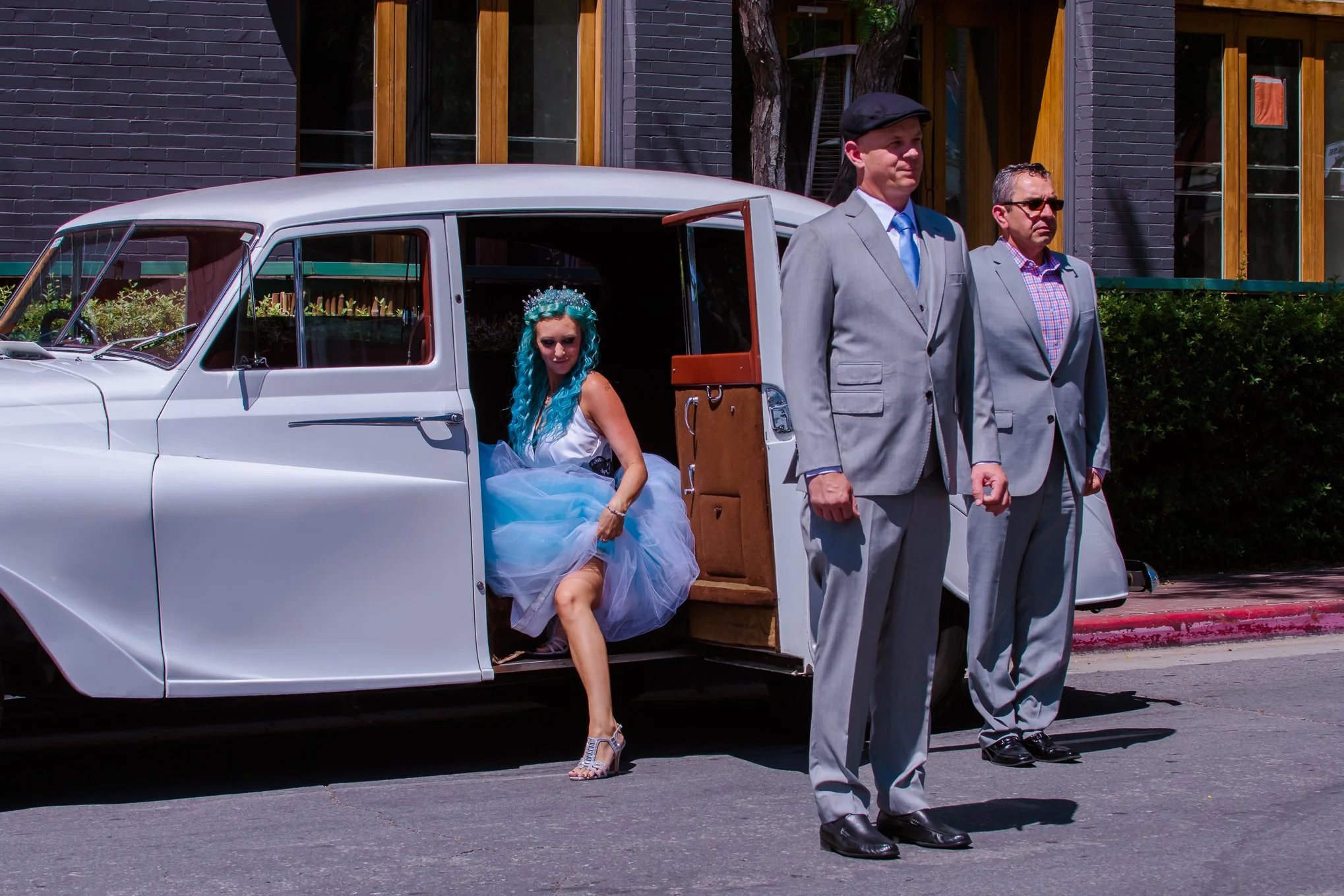 Bride with blue hair and blue dress gets out of vintage car as fiance waits for his first look