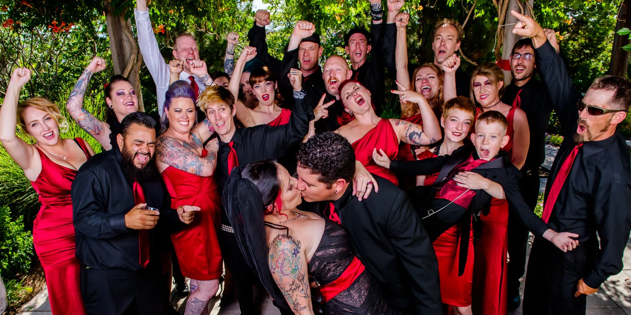 Wedding party cheer while bride and groom kiss.  Red and black attire. 
