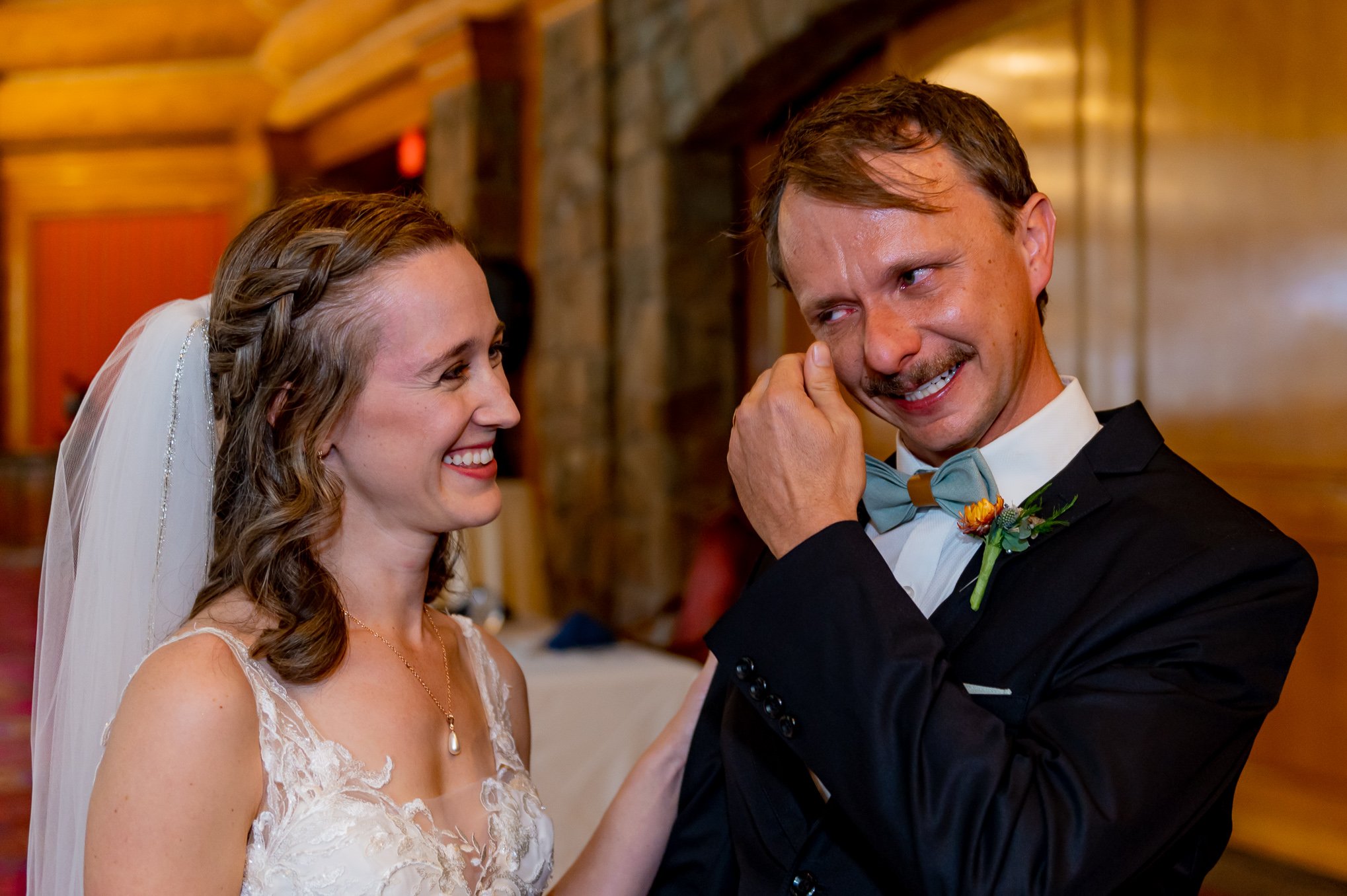 Bride laughs while her groom wipes away a happy tear during their wedding reception.