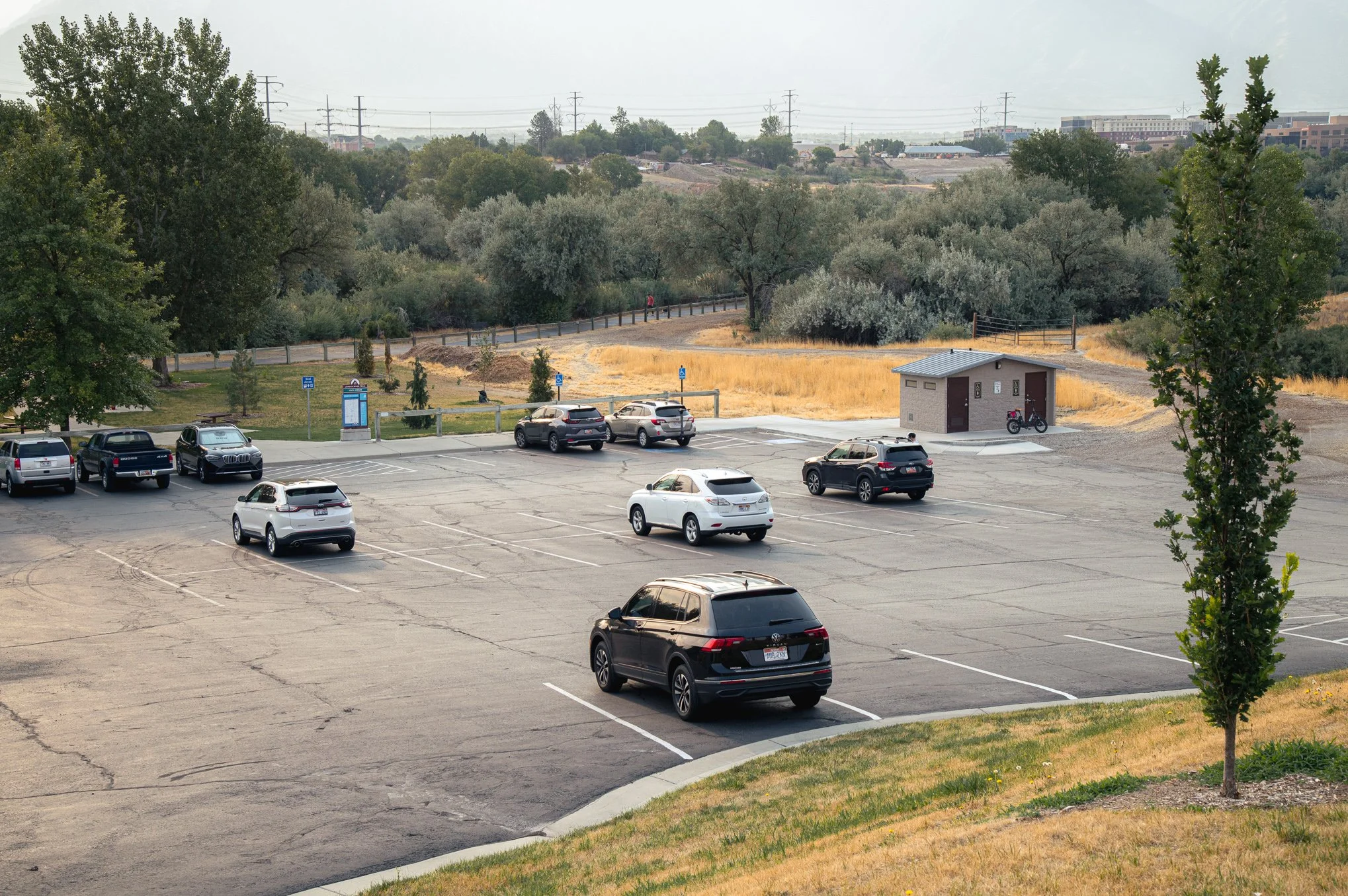 The parking lot and restrooms at Shields Lane Park in South Jordan, Utah, with the Jordan River Parkway trail beyond.