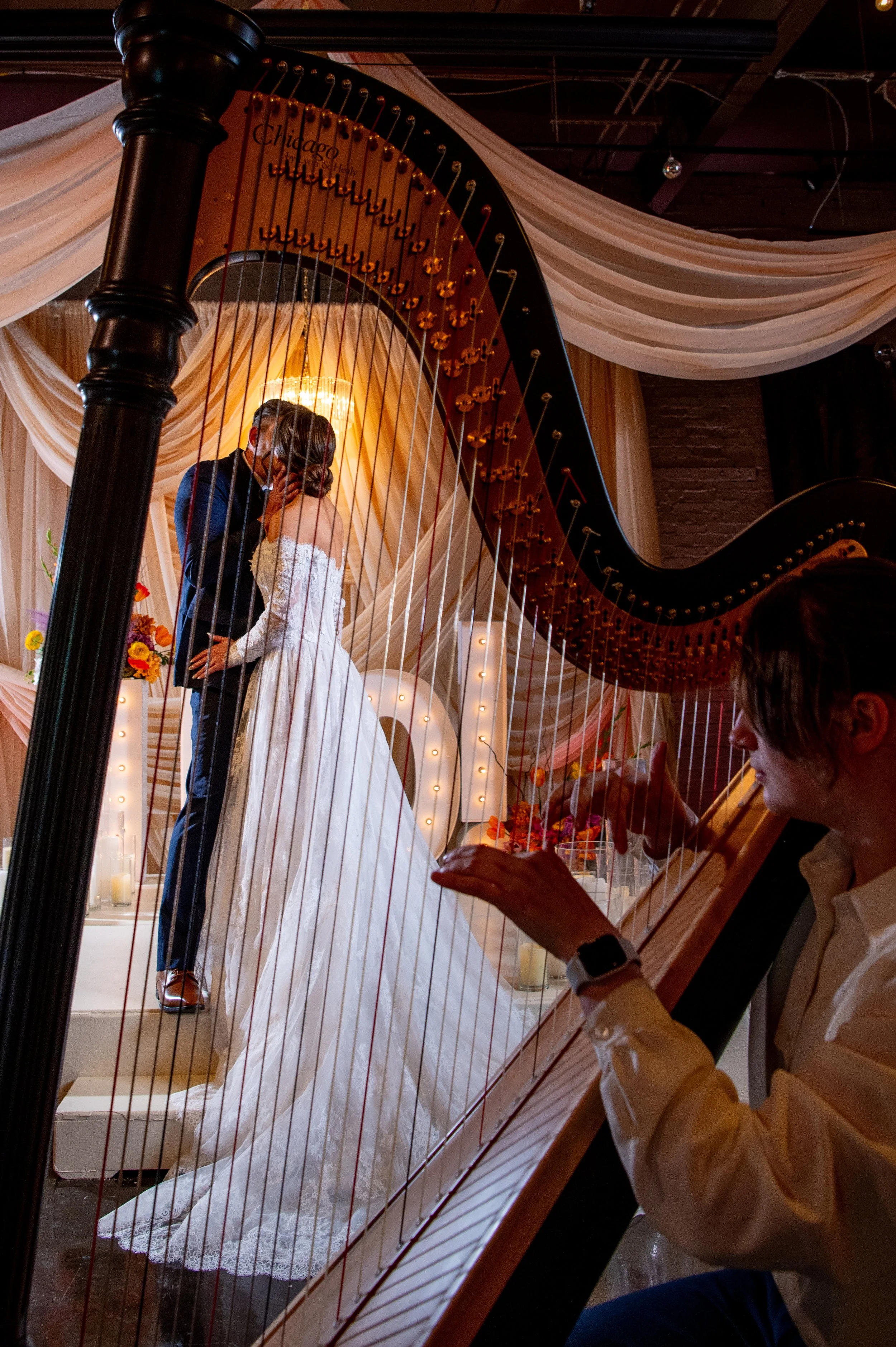 Bride and groom share their first kiss on the altar, framed through the strings of a live harp at a Utah wedding ceremony.