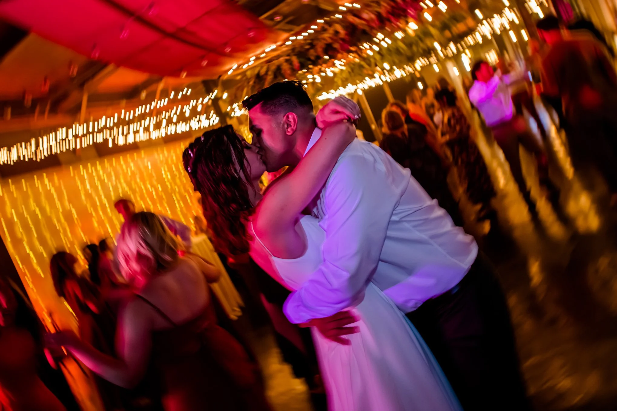 Bride and groom share a kiss on the dance floor under string lights during their wedding reception.