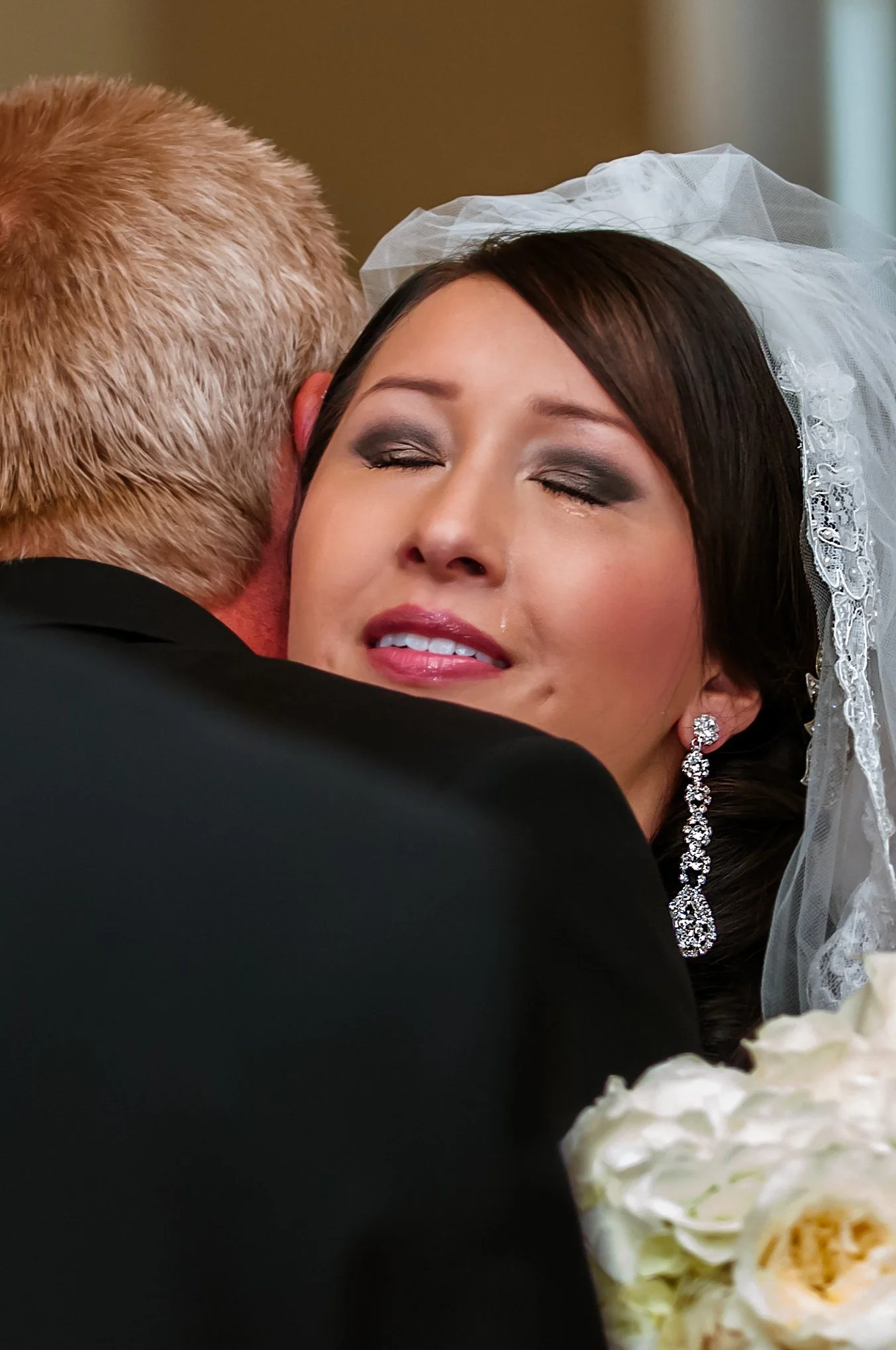 Bride tears up during an emotional embrace, veil and bouquet visible, at a Utah wedding.