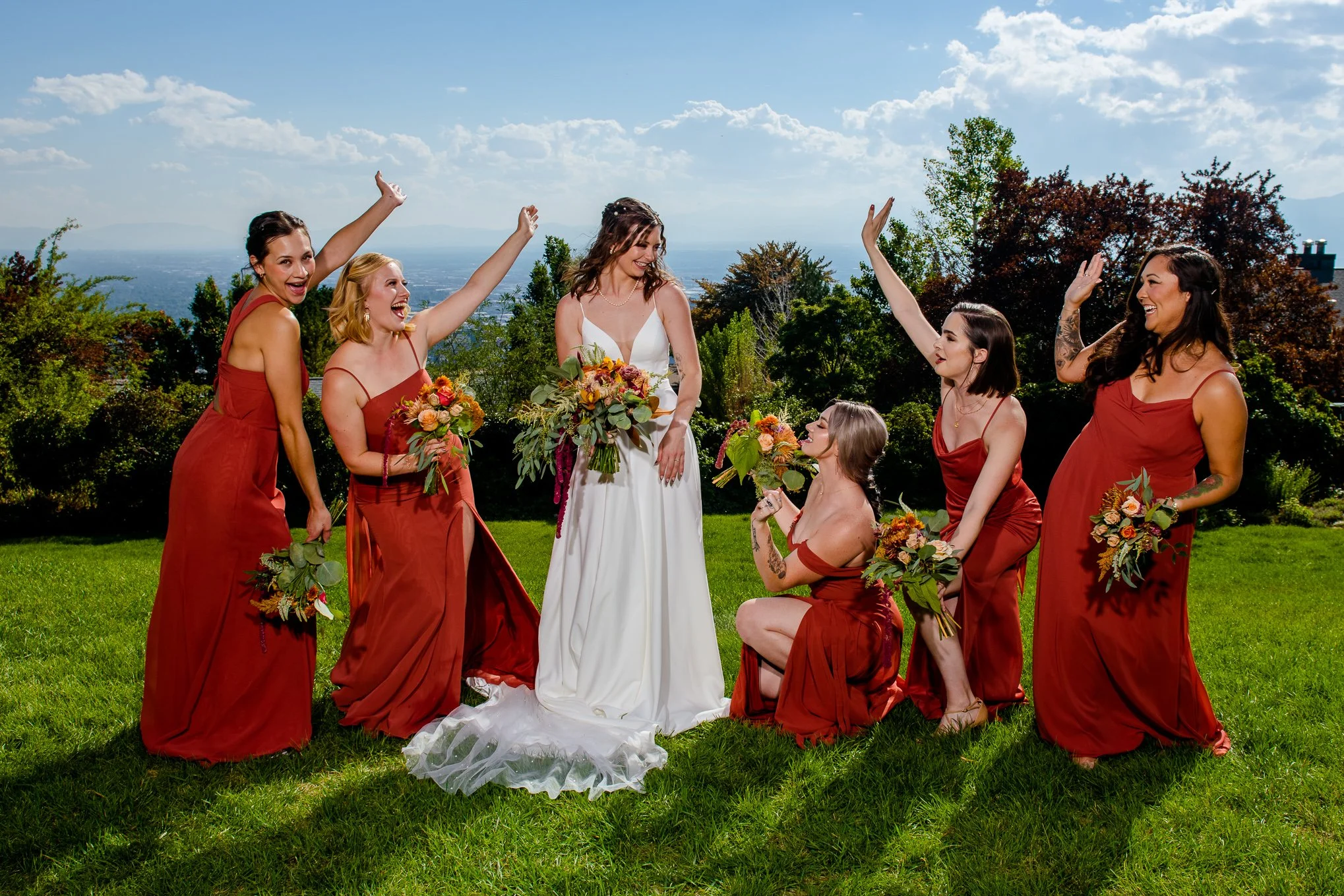Bride and her bridesmaids in rust-colored dresses cheer together with a mountain valley view behind them.