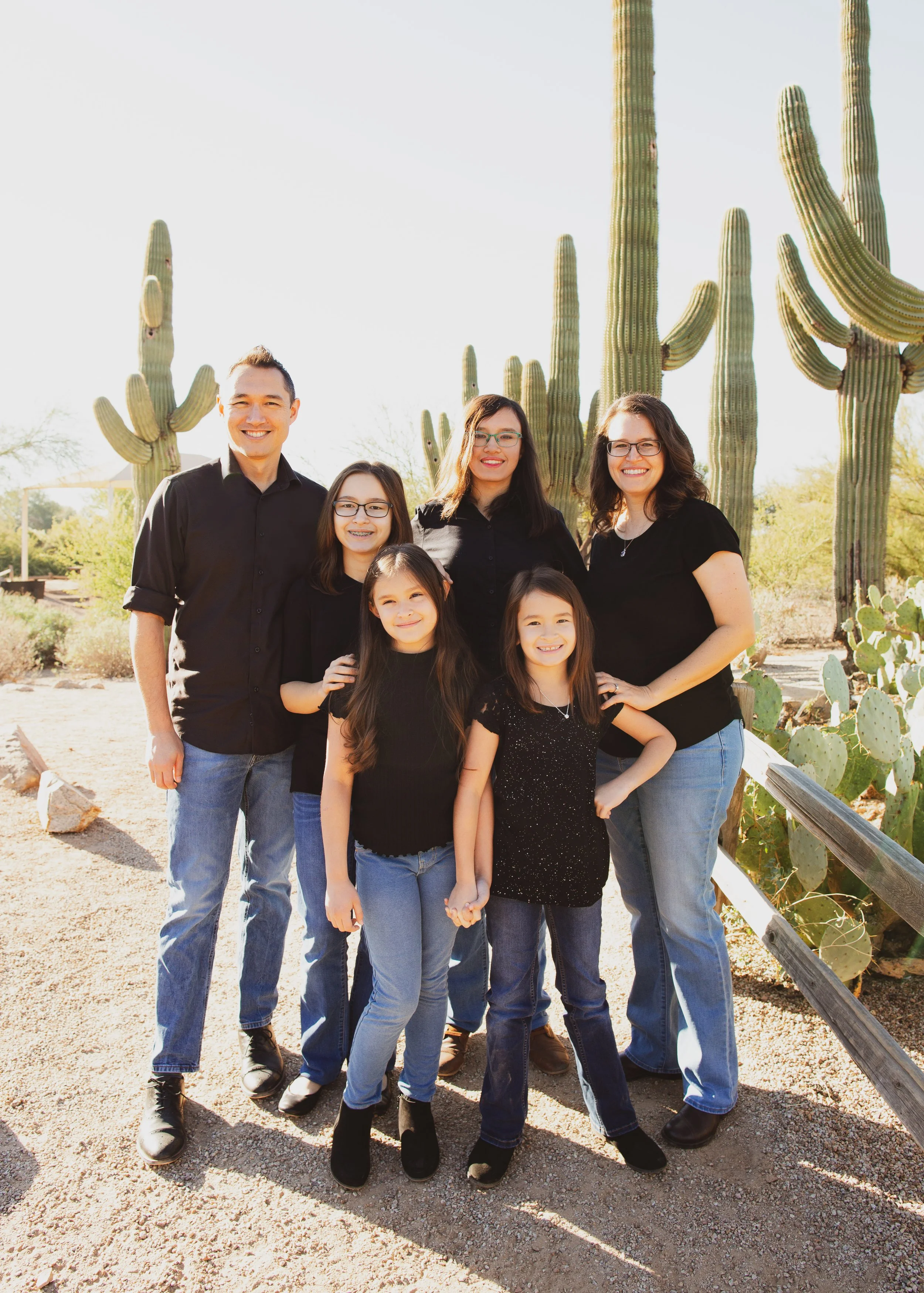 A group of seven smiling people, including men and women of different ages, standing outdoors in front of large cacti on a sunny day.
