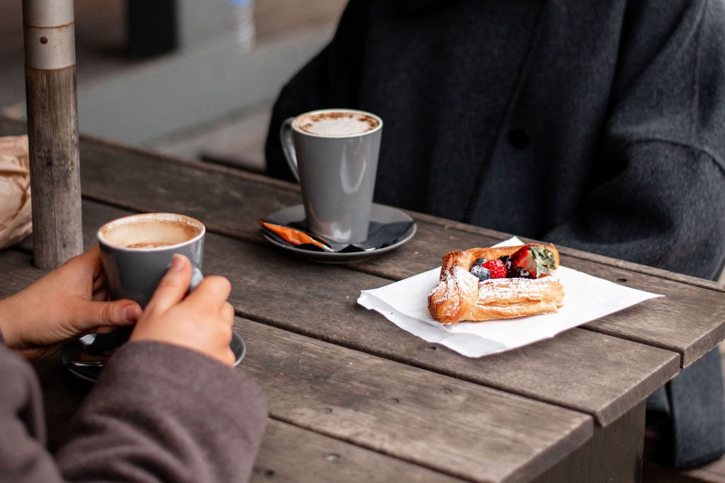Two people having hot chocolates at a rustic wooden table with pastry topped with berries.