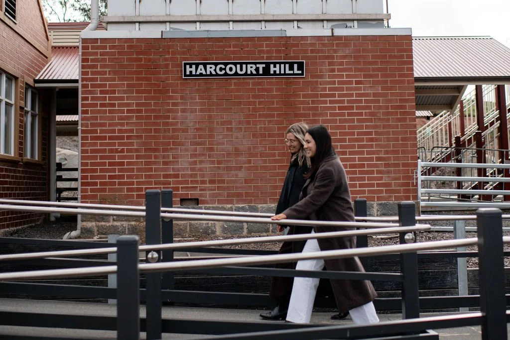 Two women walking along a walkway in front of a red brick building labeled Harcourt Hill, smiling and engaged in conversation.