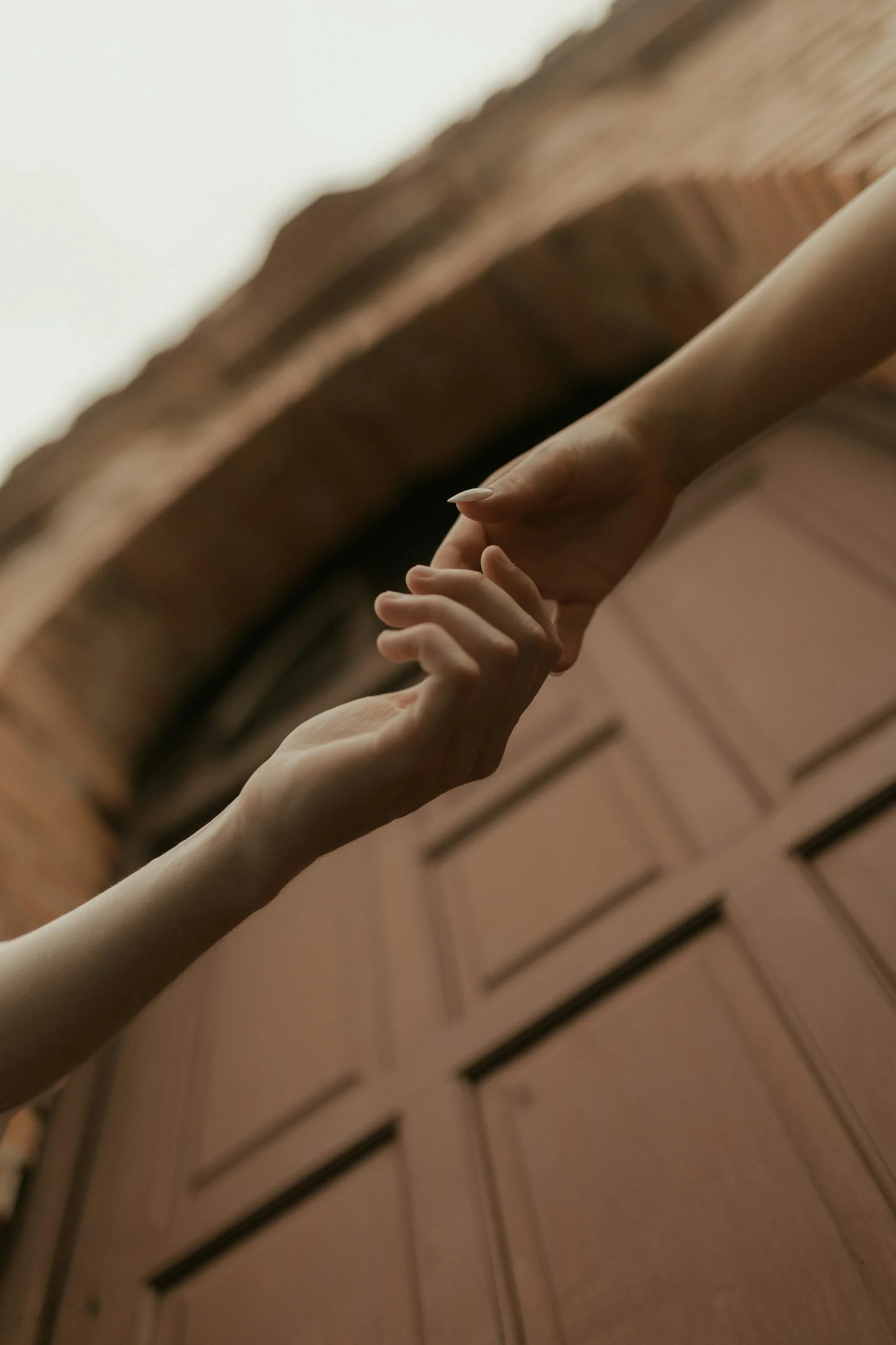 Close-up of two hands, one pale and the other darker, gently holding each other against a wooden background.