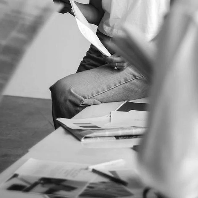 Person sitting on a chair holding papers with a stack of documents and a pen on the table in front of them.