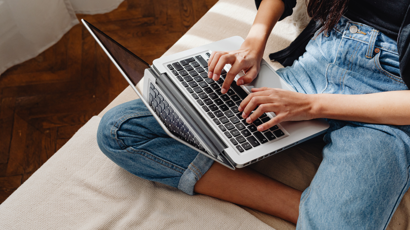 Person sitting on a bench with legs crossed, using a laptop on their lap.