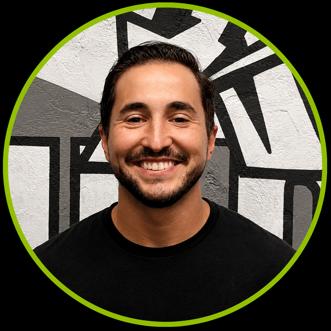 A smiling man with dark hair and a beard, wearing a black t-shirt, standing in front of a wall with black and white geometric mural, surrounded by a circular lime green border.
